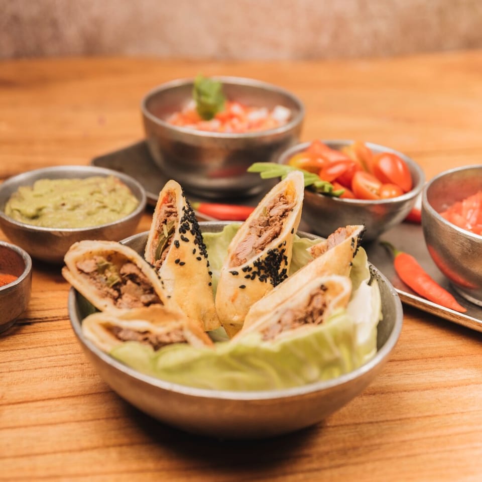 Crispy Mexican taquitos with black sesame seeds, served with guacamole, salsa, and chili peppers.