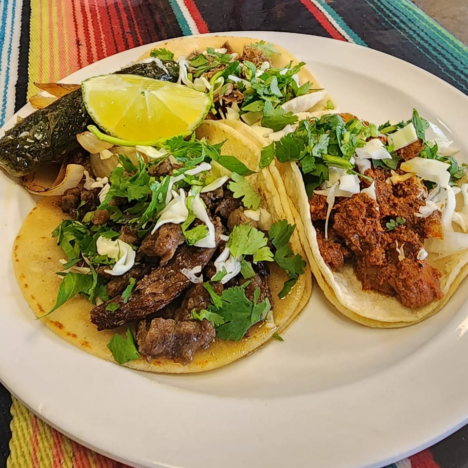 Three Don Pancho Mexican Food tacos with various fillings, cilantro, onions, lime, and a roasted pepper.